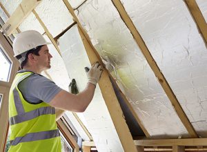A man in a white hard hat installing insulation in a roof.