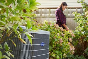 Woman in garden with heat pump in foreground.