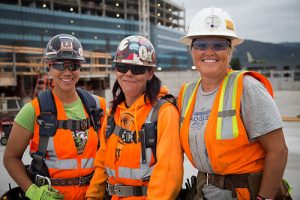 Three women workers in hardhats and orange vests