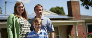 A family standing in front of their home that has solar panels on it.