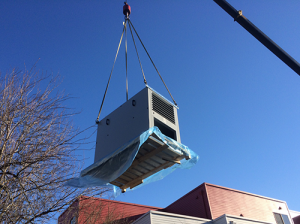 a crane lowering a machine onto a roof top for installation