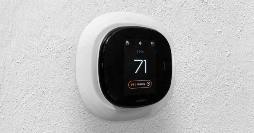 A sleek, modern ecobee smart thermostat mounted on a textured white wall, displaying a temperature of 71°F. The black front screen shows icons for Wi-Fi, lock, and flame, with a status message reading "1 Holding" below the temperature.