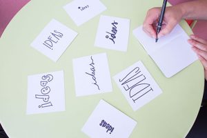 Close up of a table with pieces of paper that say "Ideas" in different fonts